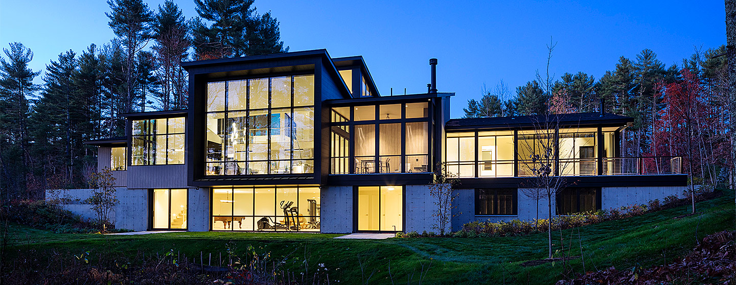 exterior night view of contemporary home with lights on and lots of glass windows