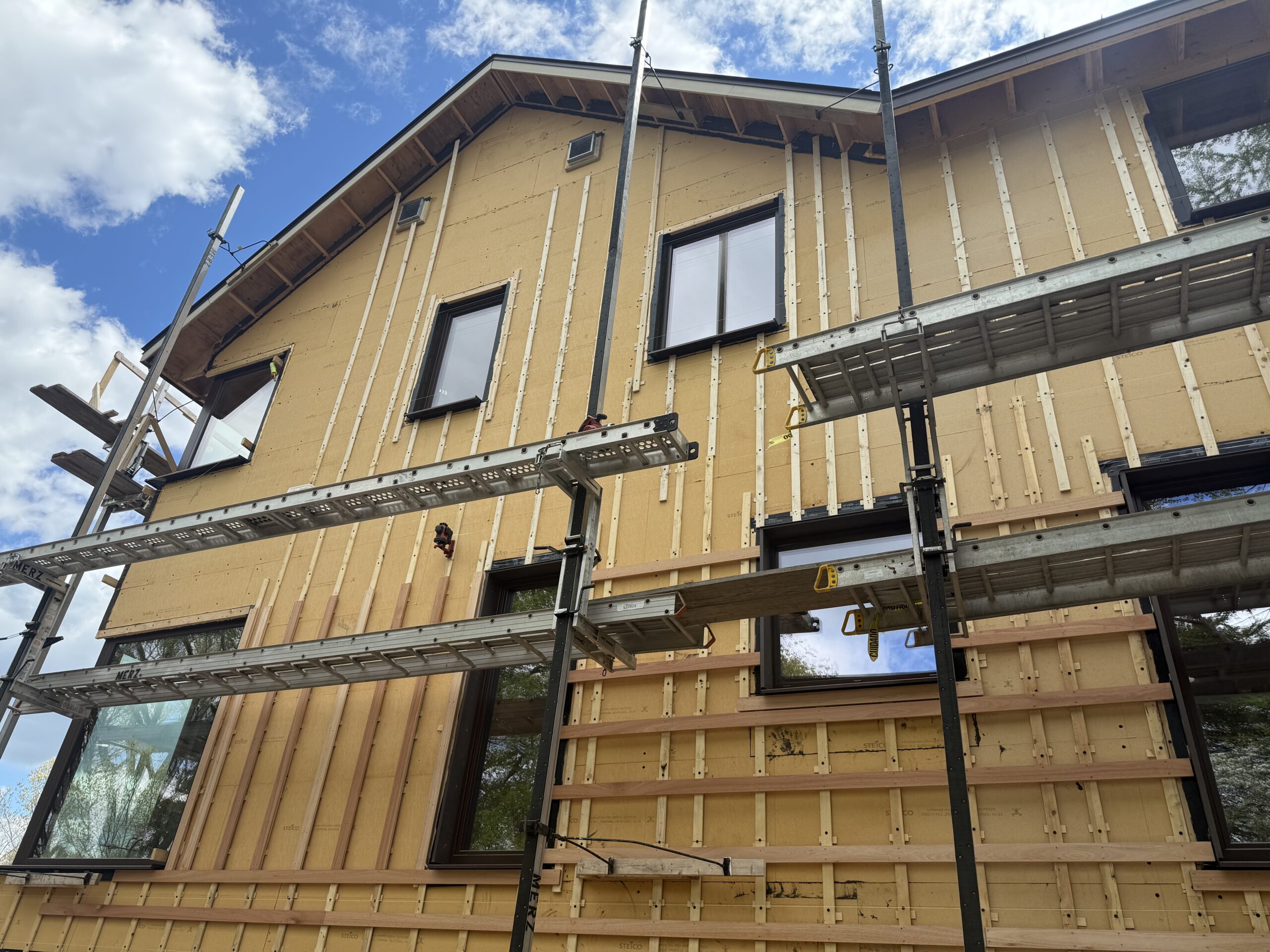 Exterior of a Lincoln, Massachusetts high-performance home under construction, with continuous wood fiber board insulation, rainscreen battens, and nickel-gap cladding being installed.