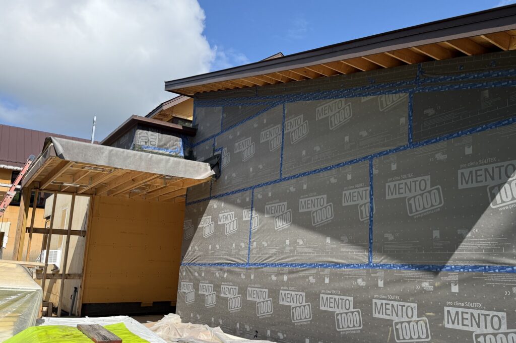 Building wrapped in Pro Clima Solitex Mento 1000 weather and air barrier membrane with Tescon Vana tape at every seam, wood fiber board and eave framing visible