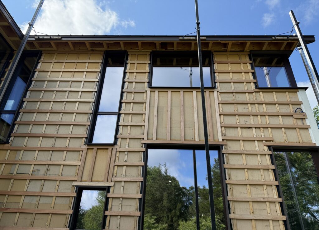 Gable elevation of a high-performance home wrapped in Steico Universal Dry wood fiber board with cross-strapped wood rainscreen battens and dark-clad triple-glazed windows